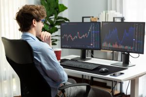 Un chico joven dos pantallas de ordenador con gráficas de trading