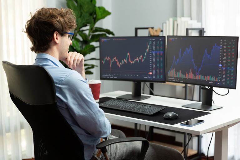 Un chico joven dos pantallas de ordenador con gráficas de trading