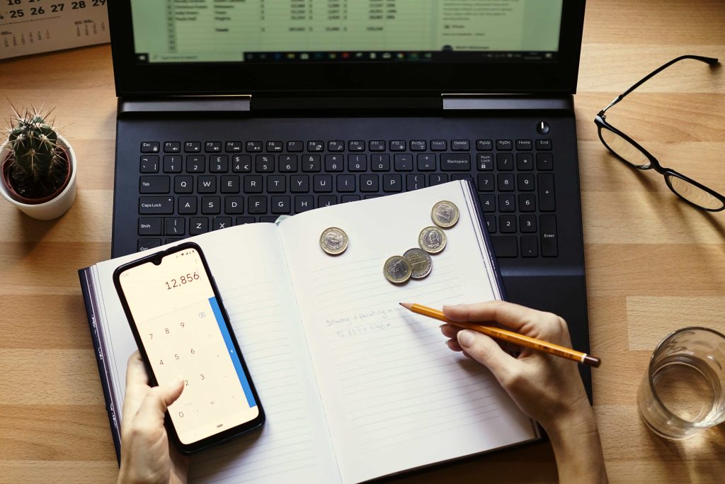 Imagen de una mesa con ordenador abierto. Encima de él una libreta con una calculadora y monedas